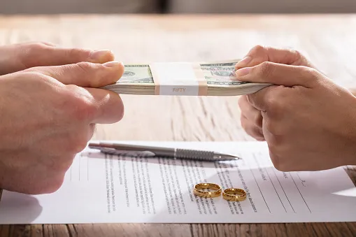 Two people pulling a stack of money from across a table.