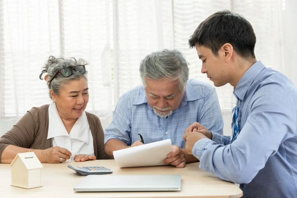 Elderly couple sitting at table with attorney, signing papers.
