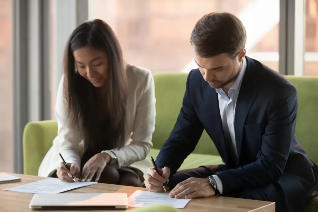 Two people signing paperwork at an office desk.