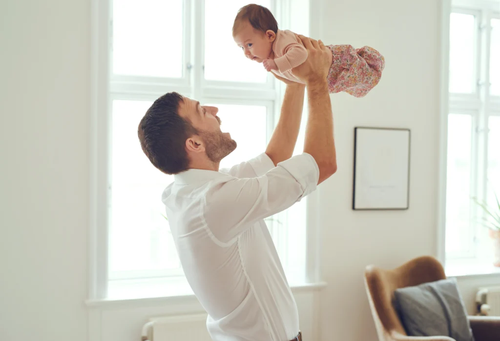 Father holding baby in the air, smiling.