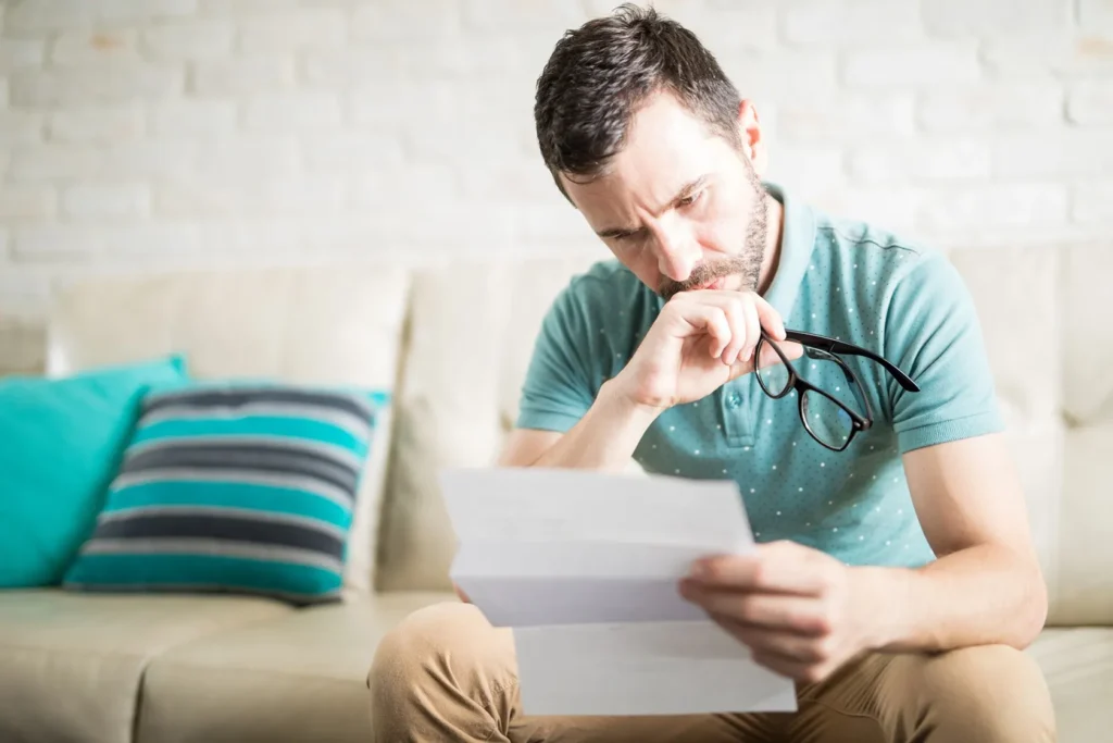A person sitting on a couch, reading a document, visible upset.