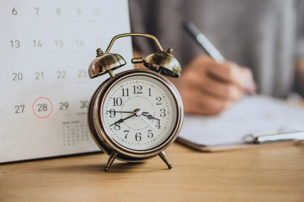 A clock and a calendar on a desk while a person works in the background.