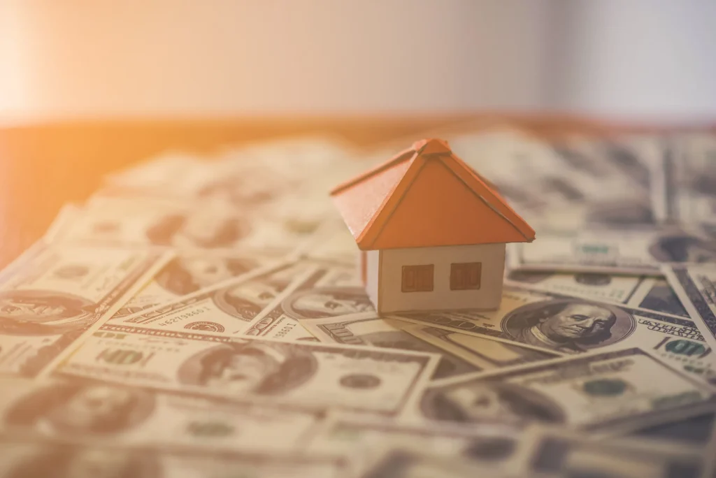 A miniature house sitting on hundred dollar bills.