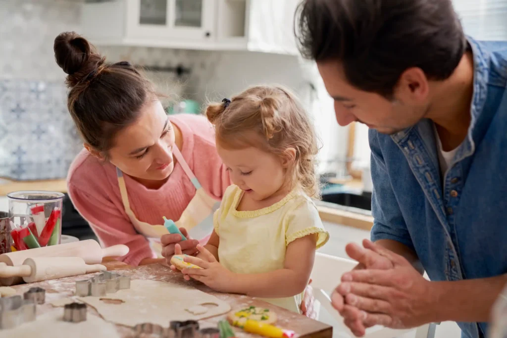 Two parents in the kitchen with their daughter making and decorating sugar cookies.