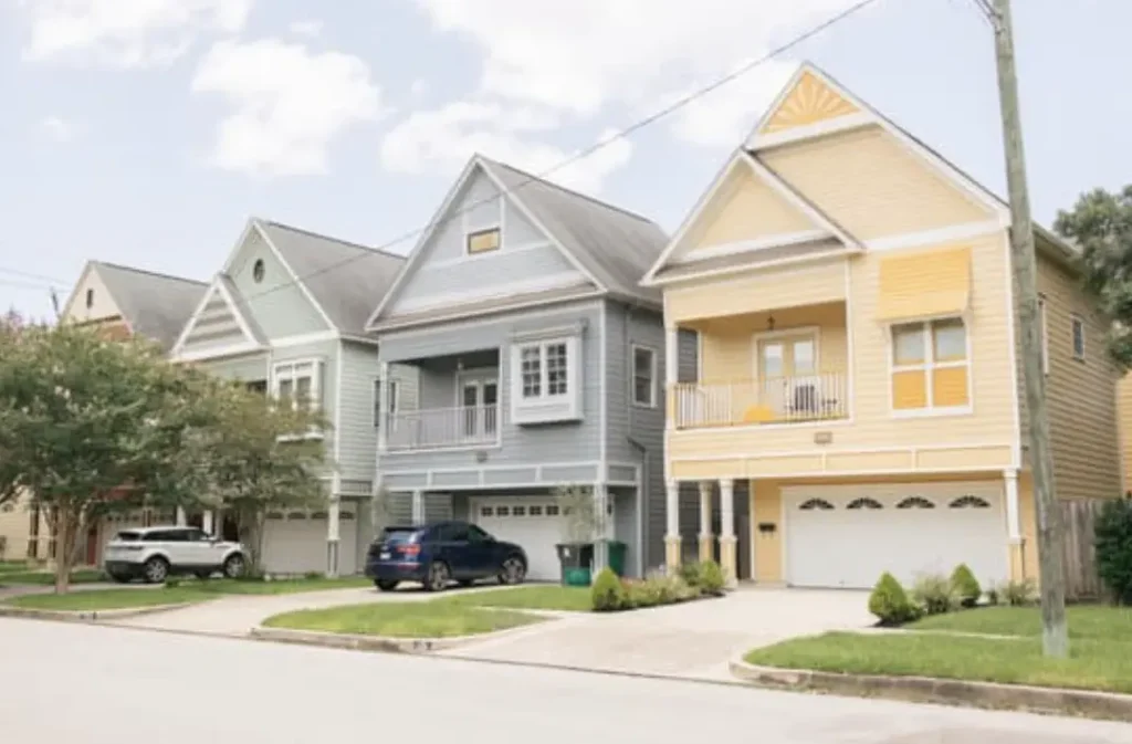 Three colorful suburban houses with driveways and front lawns on a quiet street.